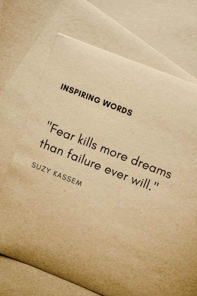 Motivational quote 'Fear kills more dreams than failure ever will.' by Suzy Kassem on paper texture.